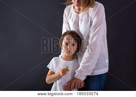 Cute little preschool boy with big bump on his head from falling hugging his mom at home and eating lollipop