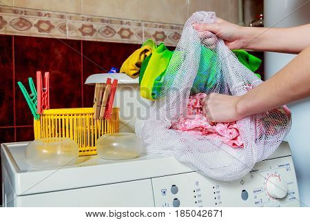 Close up top of modern washing machine in bathroom with facilities on it and female hands putting colorful cloth in wash basin