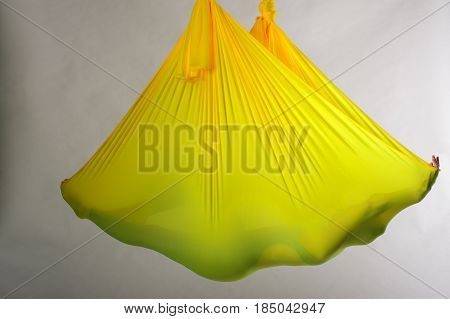 Unrecognized person lying in yellow hammock and meditating. Fly yoga practice. Body balance and antigravity training. Wellness and body care concept.