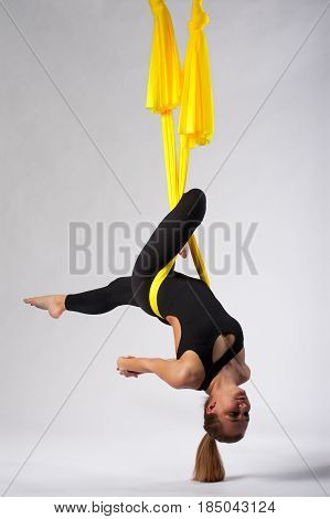 Young yogi woman doing yoga practice in yellow hammock in studio. Female blonde girl performing aero yoga or aerial acrobatics. Body balance and antigravity training. Wellness and body care concept.