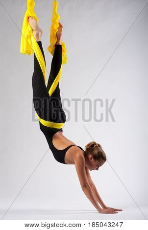 Full length portrait of young flexible woman practicing fly yoga. Fit girl working out in yellow hammock, studio shot. Body balance and antigravity training. Wellness and body care concept.