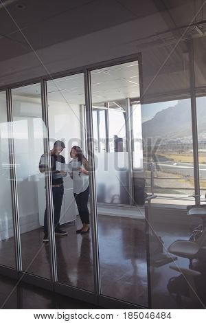 Full length of business colleagues dicussing over documets at office seen through glass