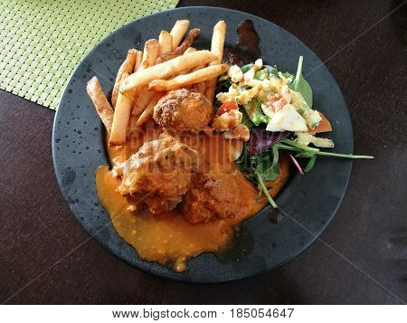 Meatballs with spicy tomato sauce on a plate side with french fries and spinach feta white cheese and tomato salad on black plate Roasted meatballs in sweet and sour tomato sauce close up top view