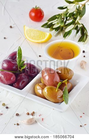 White plate with black and green olives with olive leaves on a white abstract background with lemon, cherry tomato, spices. Healthy food. Greek food. Mediterranean food