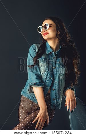 gorgeous girl in a fashionable white sunglasses, dressed in a blue jeance jacket and transparent tights without panties. posing standing near stylish transparent armchair. front view, waist portrait