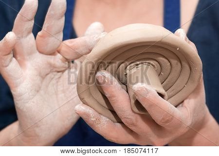 Close-up of hands of woman making clay cover pot in pottery workshop