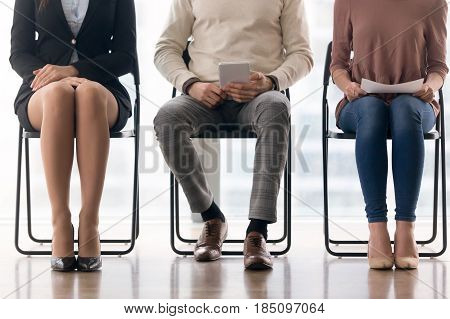 Three candidates for position waiting for their turn in job interview sitting on chairs, preparing for meeting, having audition, people in queue, human legs close up, job search concept