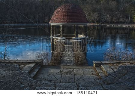 A spooky gazebo in the woods on a lake during the winter time.