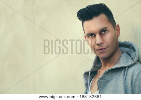 Portrait of serious young man leaning against the wall. Fashion hair style. A young man dressed in youth fashion. He is leaning against a wall and stares intently. Earnest facial expression.