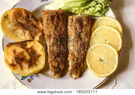 Ffried fish  baked potatoes and slices of lemon with lettuce leaf