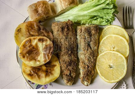 Ffried fish with bread baked potatoes and slices of lemon with lettuce leaf