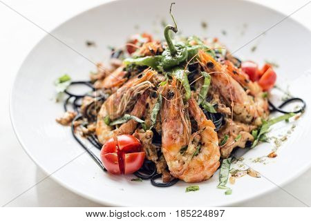 gourmet food grilled prawn and vegetables on black squid ink pasta meal