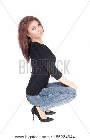 A beautiful young Caucasian woman crouching on the floor in jeans and black sweater isolated for white background.