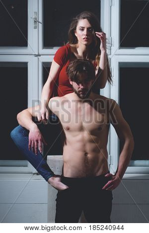 Pretty girl or beautiful woman with long blond hair in red tshirt hugging bearded man hipster or sexy bodybuilder with beard muscular torso abs biceps triceps on misted window