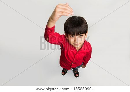 indian smart kid or boy standing over white background and showing or measuring his height with hands, looking upwards at camera, top view