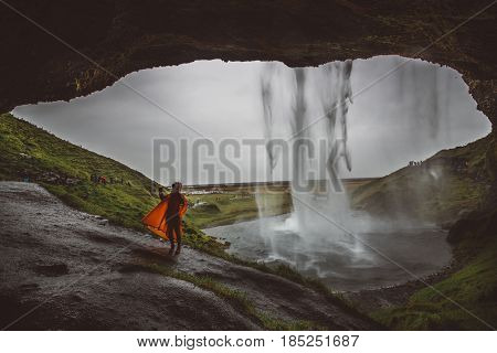 Female tourists posing in the cave hole behind big Icelandic waterfall Seljalandsfoss.Natural attractions for tourists and campers.Nature tourism.Visiting Iceland