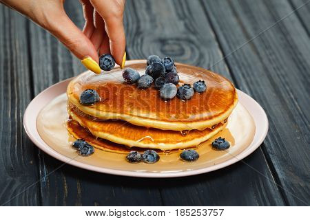 Chef garnishing a stack of pancakes with golden honey and fresh blueberries, close up of his hand and the blueberries