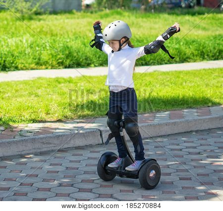 Happy small girllearned to ride electric mini hoverboard or a gyroboard in the city. She is glad and shows happy gesture