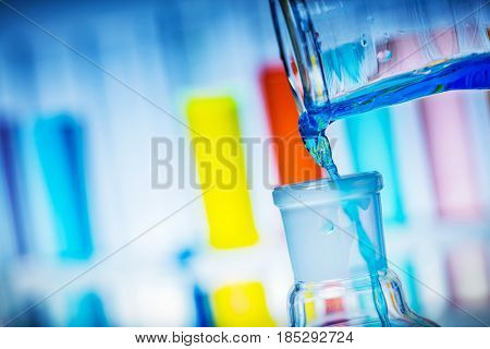 Pouring colorful liquid from tube to a flask. Chemical experiment and laboratory equipment.