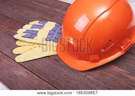 Orange hard hat and gloves for work on wood background