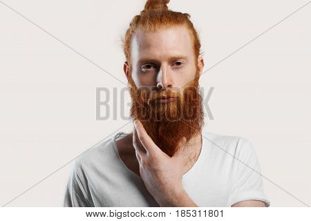 Close up portrait of red hair man with perfect skin with fleckles. Isolated portrait of attractive male with thinking emotion and hold his hot beard for relax. Kind hippie person with vegetarian view.
