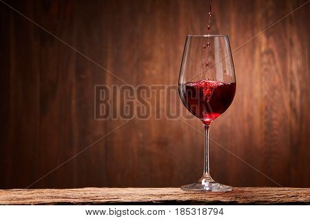 Tasty red wine poured in the elegant glass standing on the wooden stand against wooden wall background. Brightly wine and fragile goblet. Natural material and drink. Concept of the luxury lifestyle. Horizontal photo. Sommelier and tasting.