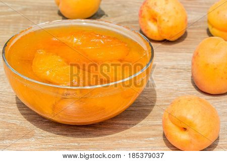 Ripe yellow apricots and homemade jam in a glass vase on a wooden table close-up. Selective focus