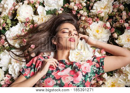Romantic and dreammy woman lying down on flowers in studio photo. Beauty concept. Floral decoration