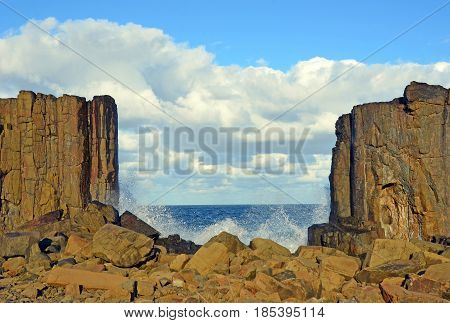 Waves breaking in the gap between basalt rock formations with a view to the sea at Bombo Headland quarry, New South Wales coast, Australia