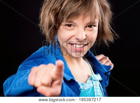 Emotional portrait of attractive caucasian little girl pointing finger to you. Funny cute smiling child 10 year old looking at camera choosing you, on black background.