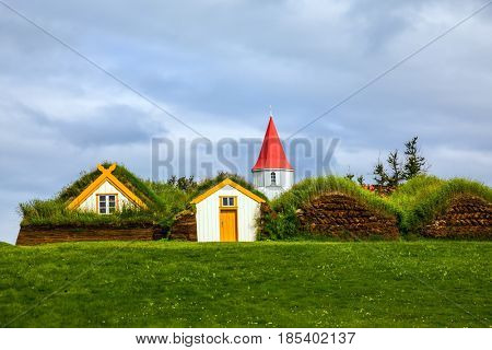 The village of old houses covered with turf and grass. Church bell tower with red gabled roof. Ethnographic Museum-estate Glaumbaer, Iceland. The concept of the historical and cultural tourism