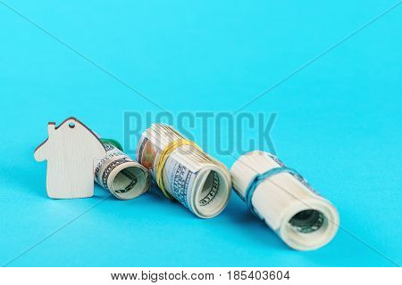 The concept of financial savings to buy a house. Mini model house dollars in rolls isolated on the blue background.