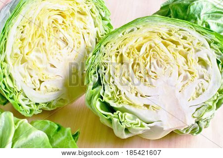 section of young fresh gren head of cabbage cutted in two parts against wooden background