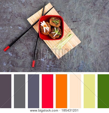 Asian meatballs, garnished with pea shoots and radish julienne, in a red bowl on bamboo tray with chopsticks. In a colour palette with complimentary colour swatches.