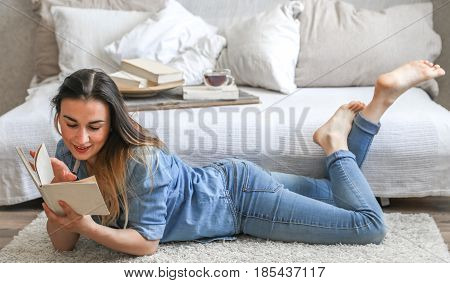 girl reading a book in a cozy room on the couch with a Cup of tea , the concept of leisure, and comfort