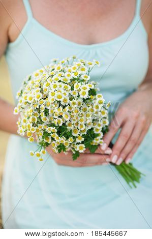 beautiful girl in a summer blue dress holds a bouquet of fresh field camomiles in hand. Tenderness, love, wedding, summer mood - concept.
