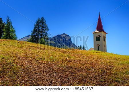 Picturesque church tower with a red roof of Maloja near St. Moritz above a meadow during summer under a clear blue sky. (Engadin Grisons Switzerland)