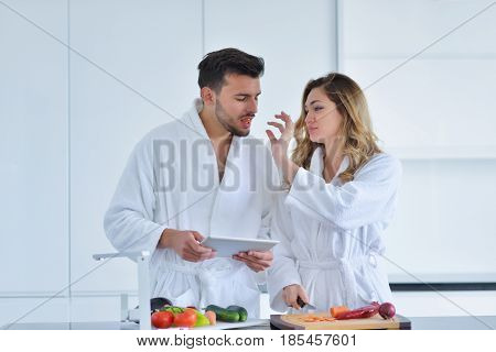 Couple in home kitchen using electronic tablet.