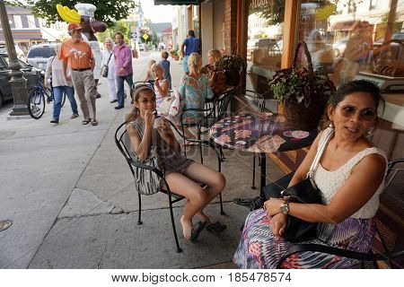 HARBOR SPRINGS, MICHIGAN / UNITED STATES - AUGUST 4, 2016: A girl enjoys eating Kilwin's ice cream, at a table outside store's front window, during the Street Musique event on Main Street in downtown Harbor Springs.