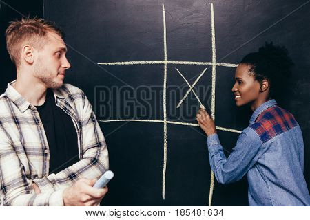 Interracial happy couple, white man and black woman play tic tac toe game. Fun leisure, great entertainment, joy and happiness, battle of the sexes concept.