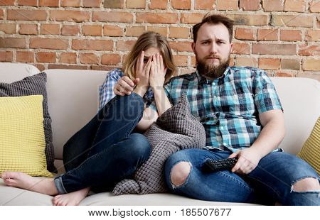 Young woman and man sitting on sofa and watching tv.