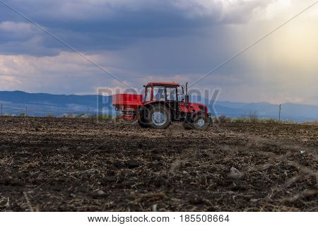 Tractor spreading artificial fertilizers in spring days