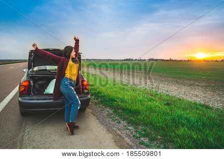 woman stratching near car on sunrise long car trip