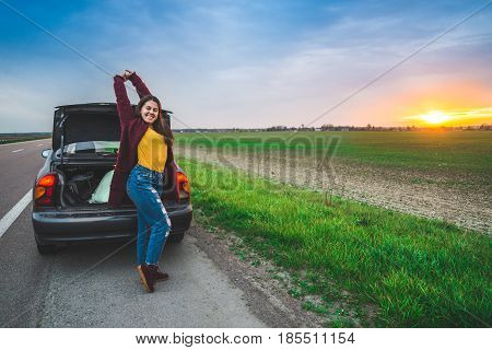 woman stratching near car on sunrise long car trip