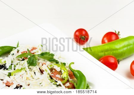 Traditional classic Shopska salad with tomatoes, peppers, cucumbers and cheese in white dish on white wooden table. Bulgarian cuisine, Balkan culture