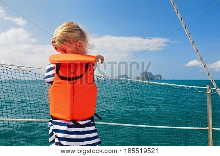 Happy little baby in life jacket on board of sailing boat watching offshore sea and tropical islands on summer cruise. Children travel adventure on family vacation. Safety during yachting with kids.