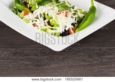 Traditional classic Shopska salad with tomatoes, peppers, cucumbers and cheese in white dish on grey wooden table. Bulgarian cuisine, Balkan culture