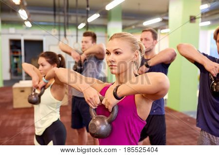 sport, fitness, weightlifting and training concept - group of people with kettlebells and heart-rate trackers exercising in gym