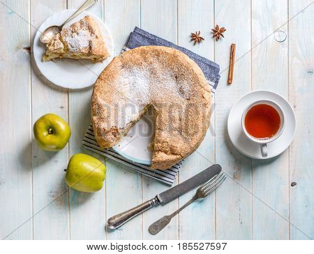 Huge hot apple pie with piece cut off, hot tea, two apples and dishwear, topshot