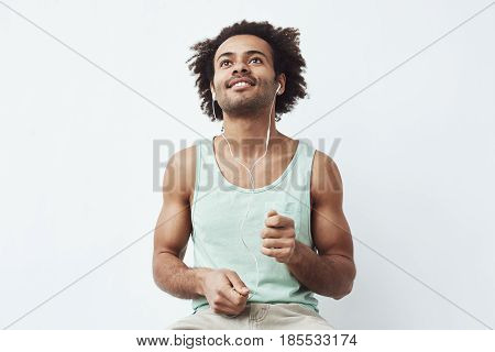 Young african man listening to music in headphones dancing over white background. Copy space.